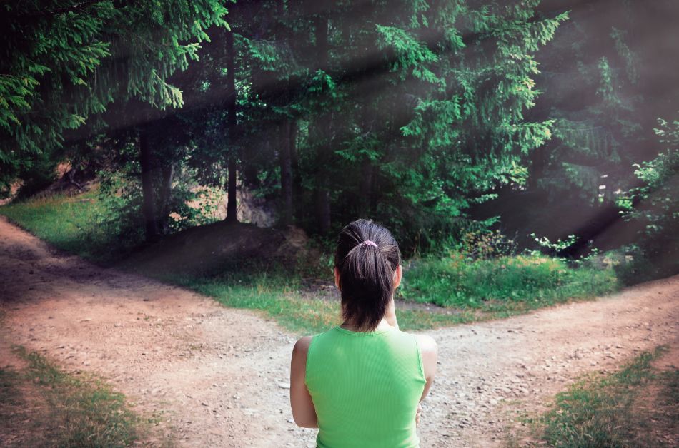 Eine Frau steht im Wald an einer Weggabelung